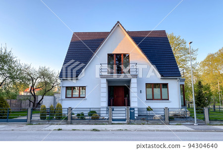 A private house of two floors with triangular roof and an area near the house against a blue sky A private house of two floors with triangular roof and an area near the house against a blue sky 94304640