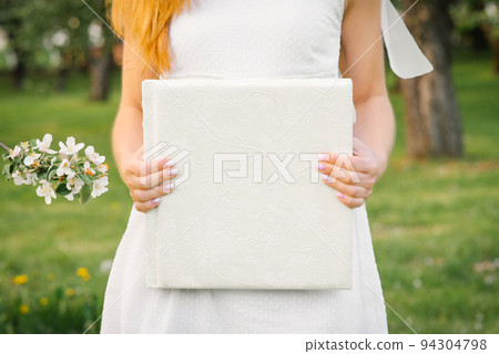 A white-covered wedding photo album is held by a woman in a white dress 94304798