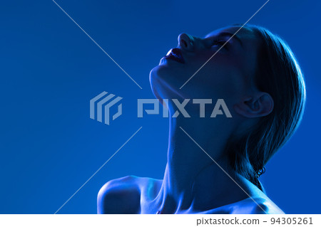 Night life. Closeup portrait of young woman in neon light on dark blue background. Monochrome. Cyberpunk style, beauty, cosmetics concept. Night life. Closeup portrait of young woman in neon light on dark blue background. Monochrome. Cyberpunk style, beauty, cosmetics concept. 94305261