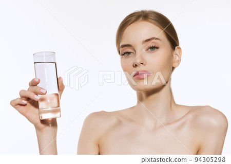 Fresh and healthy. Charming young woman with light makeup holding glass of water and looking at camera isolated over white background. 94305298