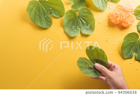 Happy Dussehra. Hand holding green leaf , yellow flowers and rice on yellow paper background. Dussehra Indian Festival concept. 94306838