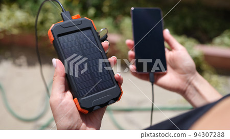 Female hand holding solar power bank and mobile phone closeup Female hand holding solar power bank and mobile phone closeup 94307288
