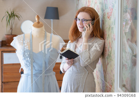 female fashion designer creates a collection of clothes in a workshop and talks on the phone. creative work of a fashion designer female fashion designer creates a collection of clothes in a workshop and talks on the phone. creative work of a fashion designer 94309168