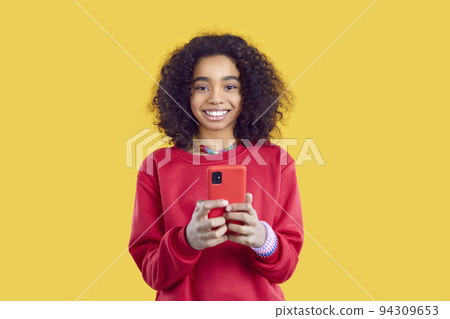 Smiling ethnic preteen girl uses modern mobile phone for online games or to communicate with friends Smiling ethnic preteen girl uses modern mobile phone for online games or to communicate with friends 94309653