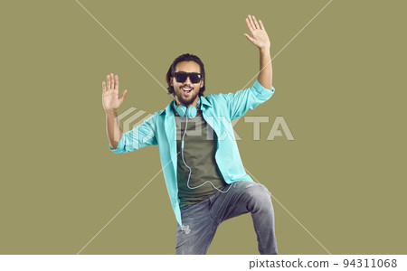 Cheerful energetic Indian man with big headphones around his neck having fun on khaki background. Cheerful energetic Indian man with big headphones around his neck having fun on khaki background. 94311068
