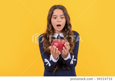 shocked child looking at red vitamin apple for lunch on yellow background, detox 94314718