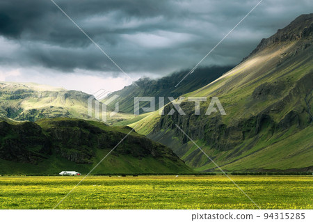 Dramatic Icelandic mountain with sunlight shining through storm clouds and house on field in summer at Iceland Dramatic Icelandic mountain with sunlight shining through storm clouds and house on field in summer at Iceland 94315285