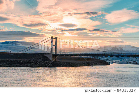 Beautiful sunset over suspension bridge on Jokulsarlon glacial river lagoon with iceberg floating in southern of Vatnajokull National Park at Iceland 94315327