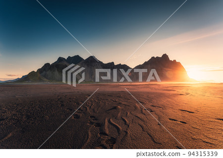 Golden sunrise on Vestrahorn mountain by atlantic ocean and black sand beach in the morning at Stokksnes peninsula, Iceland Golden sunrise on Vestrahorn mountain by atlantic ocean and black sand beach in the morning at Stokksnes peninsula, Iceland 94315339