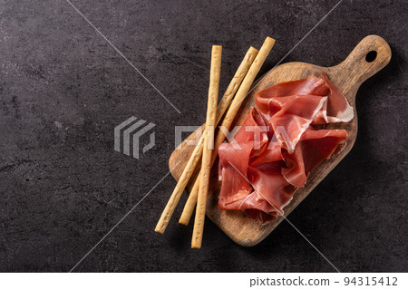Spanish serrano ham with olives and breadstick on black background Spanish serrano ham with olives and breadstick on black background 94315412