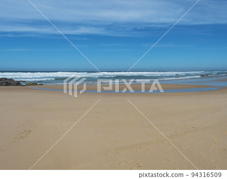 View of empty Praia do Queimado beach with ocean waves and sharp rocks and wet golden sand at wild Rota Vicentina coast near Porto Covo, Portugal. View of empty Praia do Queimado beach with ocean waves and sharp rocks and wet golden sand at wild Rota Vicentina coast near Porto Covo, Portugal. 94316509