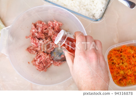 A man spices smoked paprika into minced meat in A man spices smoked paprika into minced meat in 94316878