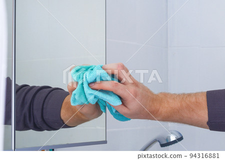 A man wipes a mirror cabinet in the bathroom with 94316881