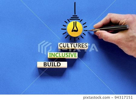 Build inclusive cultures symbol. Concept words Build inclusive cultures on wooden blocks. Businessman hand. Beautiful blue background. Business build inclusive cultures concept. Copy space. 94317151