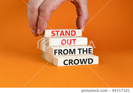Stand out from the crowd symbol. Concept words Stand out from the crowd on wooden blocks on beautiful orange table orange background. Businessman hand. Business, stand out from the crowd concept 94317181