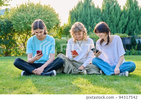 Teenage friends sitting on the grass with smartphones 94317542