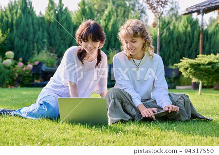 Teenage female student friends sitting on grass with laptop Teenage female student friends sitting on grass with laptop 94317550