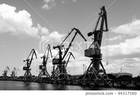 Harbor pier with many cranes and stacks of bulk cargo, coal and wood chips, black and white photo 94317560