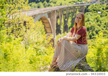 Montenegro. Woman tourist in background of Dzhurdzhevich Bridge Over The River Tara. Travel around Montenegro concept. Sights of Montenegro Portrait of a disgruntled girl sitting at a cafe table 94318933