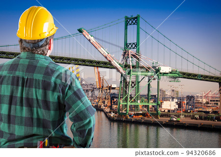 Male Worker Wearing Yellow Hard Hat Overlooking the San Pedro Ship Yard and Bridge. Male Worker Wearing Yellow Hard Hat Overlooking the San Pedro Ship Yard and Bridge. 94320686