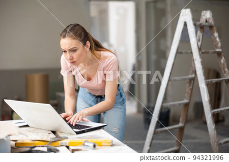 Owner of cottage checks the completion of repair work using laptop 94321996