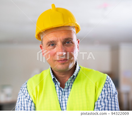 Portrait of smiling worker in yellow vest and hard hat inside cottage under renovation Portrait of smiling worker in yellow vest and hard hat inside cottage under renovation 94322009