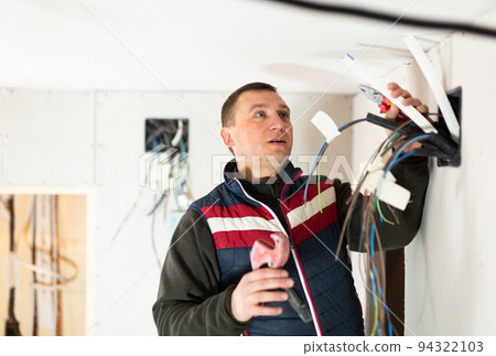 Professional builder engaged in electrical installation work at indoors building site 94322103
