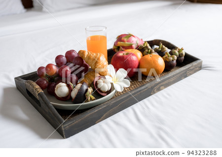 Breakfast, fruit, croissants, orange juice, in a black wooden tray, on a white bedsheet, Healthy food concept Breakfast, fruit, croissants, orange juice, in a black wooden tray, on a white bedsheet, Healthy food concept 94323288