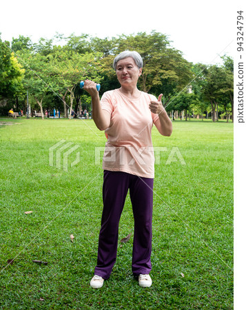 Portrait of mature asian woman 60s wearing sports clothing doing arm work out and lifting dumbbell exercise with relaxation for healthy in park outdoor. Portrait of mature asian woman 60s wearing sports clothing doing arm work out and lifting dumbbell exercise with relaxation for healthy in park outdoor. 94324794