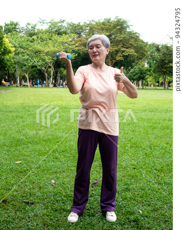 Portrait of mature asian woman 60s wearing sports clothing doing arm work out and lifting dumbbell exercise with relaxation for healthy in park outdoor. Portrait of mature asian woman 60s wearing sports clothing doing arm work out and lifting dumbbell exercise with relaxation for healthy in park outdoor. 94324795