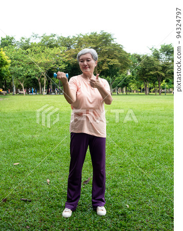 Portrait of mature asian woman 60s wearing sports clothing doing arm work out and lifting dumbbell exercise with relaxation for healthy in park outdoor. Portrait of mature asian woman 60s wearing sports clothing doing arm work out and lifting dumbbell exercise with relaxation for healthy in park outdoor. 94324797