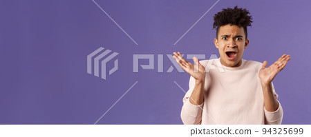 Close-up portrait of displeased, bothered frustrated hispanic man spread hands sideways in dismay and confusion, staring camera upset with disappointed grimacing expression, purple background 94325699