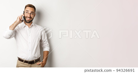 Successful business man in glasses talking on mobile phone, looking satisfied and smiling, standing against white background 94326691