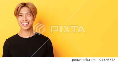 Close-up of handsome stylish asian guy with fair hair, smiling happy over yellow background 94326712