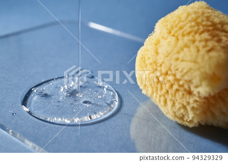 A natural sponge and a drop of gel or shampoo on a blue background. 94329329
