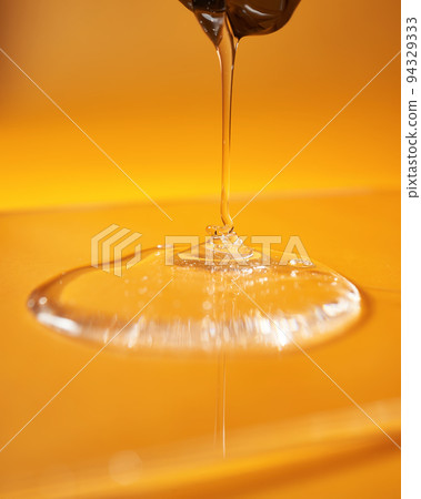 A drop of body gel or shampoo pouring from above on a yellow saturated background. A drop of body gel or shampoo pouring from above on a yellow saturated background. 94329333