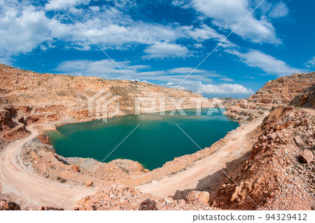 Emerald lake in a flooded quarry. Emerald green lake in flooded opencast mine, open pit. Oval lake in mining industrial crater, acid mine drainage in rock. Open pit mine with lake. Kadykovskiy quarry 94329412