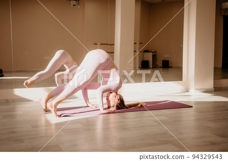 Young sporty woman, fitness instructor in pink sportswear doing stretching and pilates on yoga mat in the studio with mirror. Female fitness yoga routine concept. Healthy lifestyle and harmony. Young sporty woman, fitness instructor in pink sportswear doing stretching and pilates on yoga mat in the studio with mirror. Female fitness yoga routine concept. Healthy lifestyle and harmony. 94329543