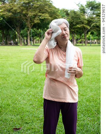 快樂的樂齡亞洲婦女微笑著站在草地上,脖子披著運動毛巾,享受公園裡的大自然新鮮空氣. 快樂的樂齡亞洲婦女微笑著站在草地上,脖子披著運動毛巾,享受公園裡的大自然新鮮空氣. 94329657