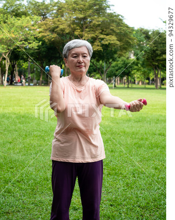 Happy senior asian woman smiling and using dumbbells while standing on grass and enjoying nature fresh air in park. Happy senior asian woman smiling and using dumbbells while standing on grass and enjoying nature fresh air in park. 94329677