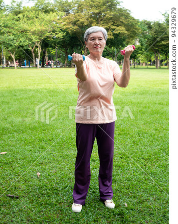 Happy senior asian woman smiling and using dumbbells while standing on grass and enjoying nature fresh air in park. Happy senior asian woman smiling and using dumbbells while standing on grass and enjoying nature fresh air in park. 94329679