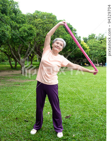 Pleasant entertainment at the airport, where women smile and use the power belt exercise on the grass, as well as enjoy the fresh air of nature in the park. 94329704