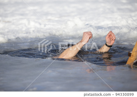 A man plunges into an ice-hole during the winter festival of the baptism of Jesus. A man swims in the ice-hole in winter. Walrus people. 94330899