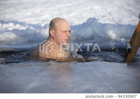 A man plunges into an ice-hole during the winter festival of the baptism of Jesus. A man swims in the ice-hole in winter. Walrus people. A man plunges into an ice-hole during the winter festival of the baptism of Jesus. A man swims in the ice-hole in winter. Walrus people. 94330907