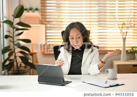 Mature businesswoman having video conference, virtual meeting on digital tablet. Distant communication, remote workday concept Mature businesswoman having video conference, virtual meeting on digital tablet. Distant communication, remote workday concept 94331058