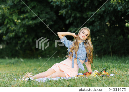A beautiful young woman is sitting on a blanket on the grass. Summer picnic A beautiful young woman is sitting on a blanket on the grass. Summer picnic 94331675