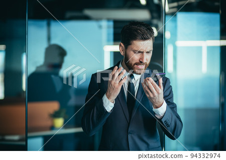 Angry and nervous boss shouting into phone, during phone conversation with employee, businessman in modern office with phone Angry and nervous boss shouting into phone, during phone conversation with employee, businessman in modern office with phone 94332974