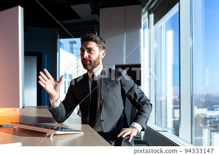 Businessman with a beard working in the office, a man talking on a video call, looking at the webcam, and talking, having fun gesturing with his hands 94333147