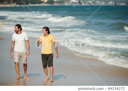 Positive male friends enjoying walking on sea beach on sunny day Positive male friends enjoying walking on sea beach on sunny day 94334272