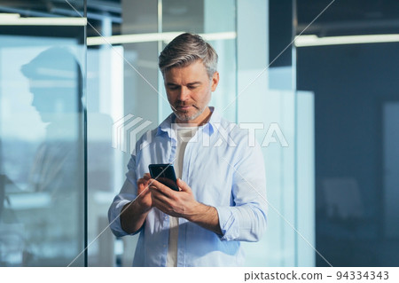 Senior boss business man in modern office, portrait of business owner using phone smiling and rejoicing Senior boss business man in modern office, portrait of business owner using phone smiling and rejoicing 94334343